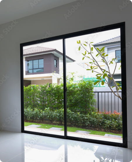 ガラス扉越しに緑の庭と住宅の屋根が見える明るいリビングからの眺め