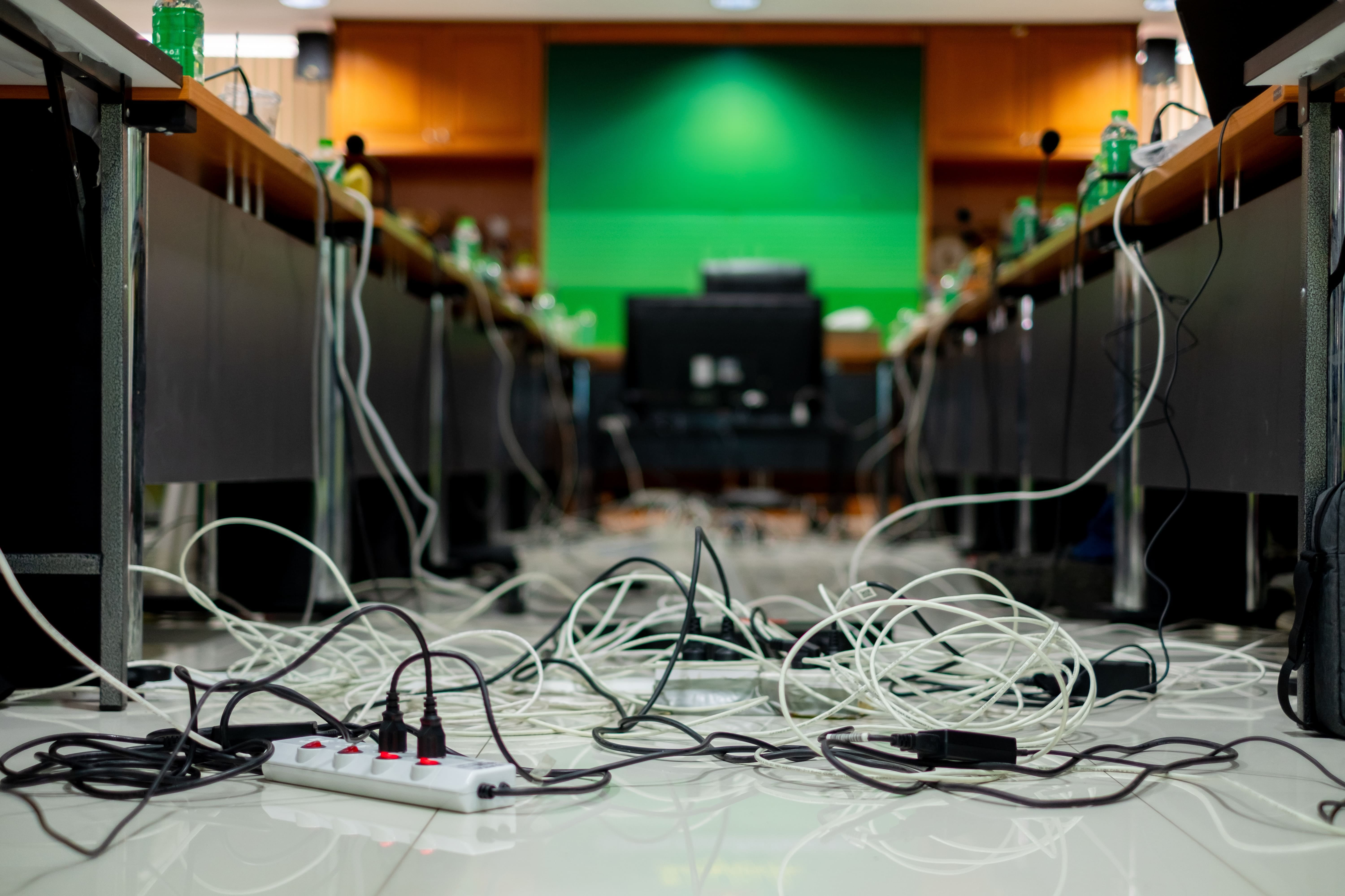 会議室の床に広がる白黒のケーブルと電源タップが散らばった配線の様子